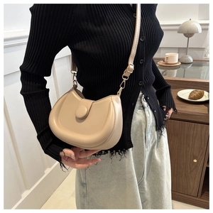 Detail of a beige crescent crossbody bag with a round flap clasp and slim strap