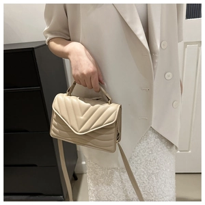Detailed view of beige quilted handbag with gold hardware and V-shaped stitching pattern