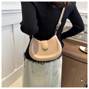 Close-up of minimalist beige crescent crossbody bag worn by model in a cozy cafe