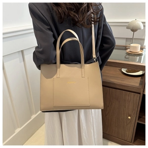 Detail of a large beige PU leather tote bag with elegant gold lettering on the front pocket