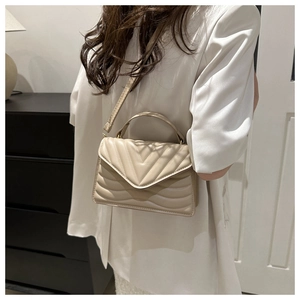 Detail view of beige chevron quilted crossbody bag with top handle and thin strap