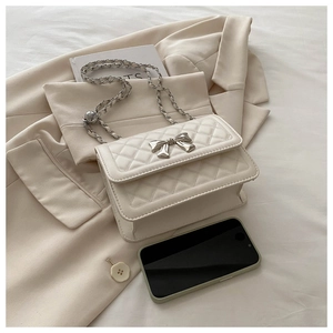 Detail of cream quilted crossbody bag with metal bow clasp and gold chain strap