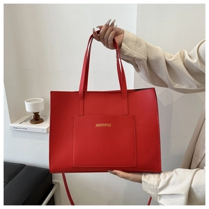 Detail of red faux leather tote bag with gold logo lettering and large front pocket