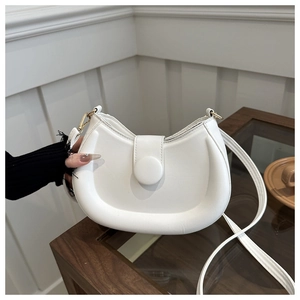 Detail of white crescent moon bag with padded texture and round decorative buckle