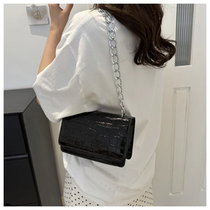 Detail of black crocodile texture leather crossbody bag with silver chain strap on a model