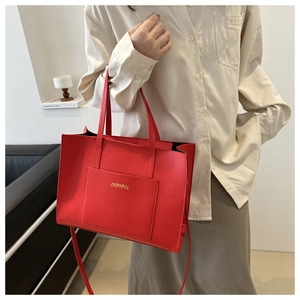 Close-up of red leather tote bag showing front pocket and adjustable shoulder strap