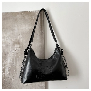 Detail of glossy black patent leather tote with embossed text and metallic chain straps