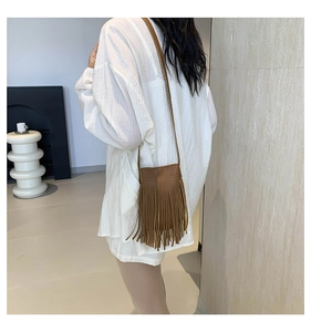 Close-up of caramel brown tassel crossbody bag shown on a model in a minimalist setting