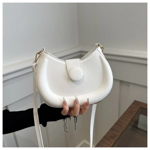 Close-up of white faux leather saddle bag featuring a gold metal hook and magnetic snap