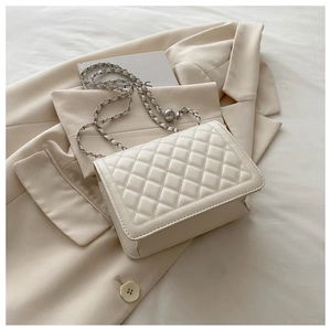 Detail of quilted leather crossbody bag with chain strap on a stylish beige blazer