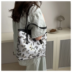 Detail of a white canvas tote bag with butterfly embroidery and black leather straps