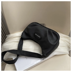 Detail of a black pleated crescent underarm bag on a white silk background