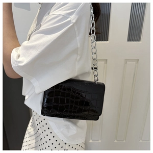 Detail of black faux crocodile skin texture and chunky silver chain on a crossbody bag