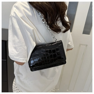 Detail of black crocodile texture flap bag with silver chain strap worn by a model