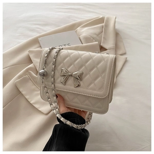Detail of off-white quilted crossbody bag with silver metal bow clasp and chain strap