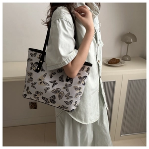 Detail of canvas tote bag featuring butterfly embroidery and sleek black leather straps
