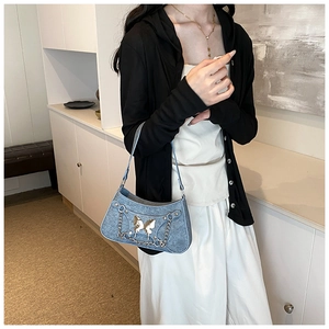 Detalle de bolso de hombro denim azul con dije de mariposa plateada y cadena fina