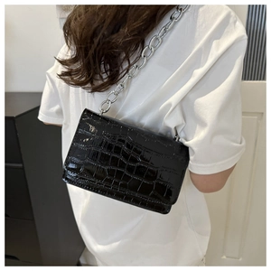 Detail of black crocodile texture patent leather crossbody bag with silver chain strap