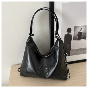 Detail of black tote bag with embossed lettering and metallic chain strap on wooden surface
