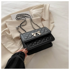 Detail of black quilted crossbody bag with silver bow accent and metal chain strap