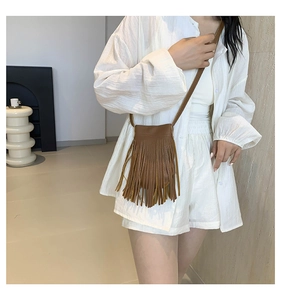 Detailed view of a brown faux leather crossbody bag with long fringes in bohemian style
