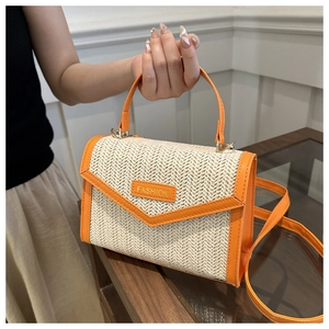 Détail d'un sac en paille tissée avec bordure en cuir orange et plaque logo tendance