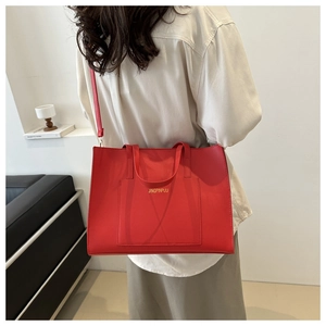 Detailed view of red tote bag with top handle and adjustable shoulder strap on model