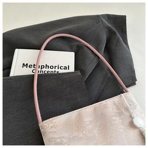 Details einer rosa Jacquard-Handtasche aus Satin mit Blumenanhänger und dünnem Riemen