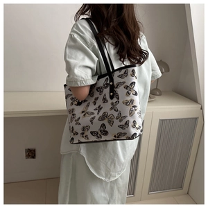 Detail of a beige tote bag with black and gold butterfly embroidery and leather straps