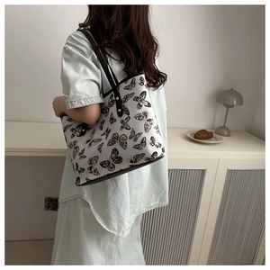 Detailed view of white tote bag with black butterfly prints and metal rivet accents