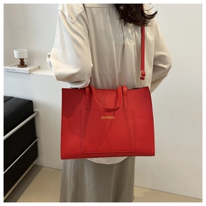 Detail of red tote bag featuring gold lettering logo and textured faux leather surface