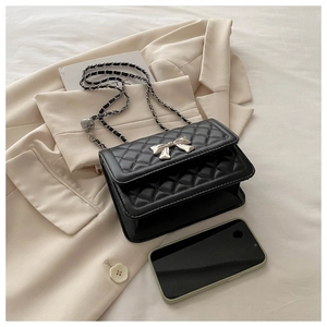 Detail of black quilted crossbody bag with silver bow accent and metal chain strap