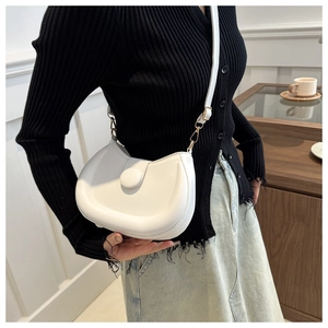 Detailed view of white semi-circular shoulder bag with gold hardware on a casual outfit