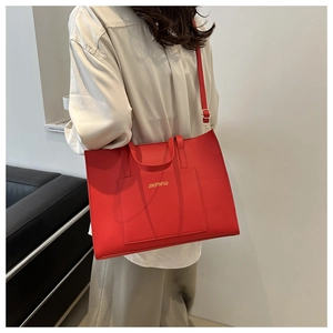 Detail of red leather tote bag with gold hardware and adjustable crossbody strap on model