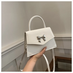 Detail of white glossy leather handbag featuring a stylish silver metal bow decoration