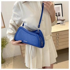 Unique asymmetrical navy blue leather shoulder bag with gold logo on model in stylish room