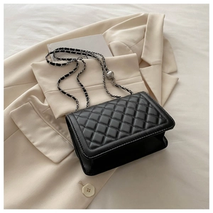 Detail of black quilted leather shoulder bag with silver metal ball chain on a beige blazer