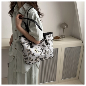 Detail of butterfly print tote bag showing black shoulder straps and gold rivet accents