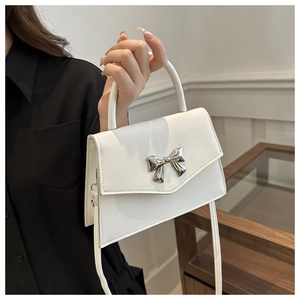 Detail of white mini bow handbag with glossy finish and detachable shoulder strap