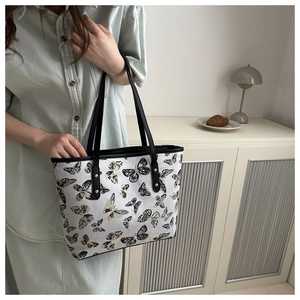 Detail of elegant tote bag with embroidered butterfly patterns and black shoulder straps