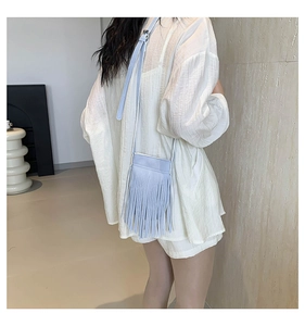 Detailed back view of a light blue tassel crossbody phone bag on a model in minimalist setting