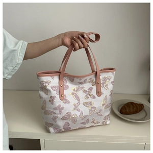 Detail of pink butterfly embroidery on a white tote bag with faux leather handles