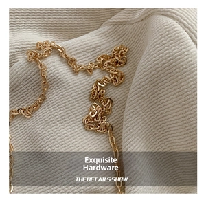 Macro shot of polished gold metal chain strap on textured beige knit fabric background