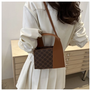 Detailansicht der braunen Handtasche mit Monogramm und Lederbesatz auf Holzschrank