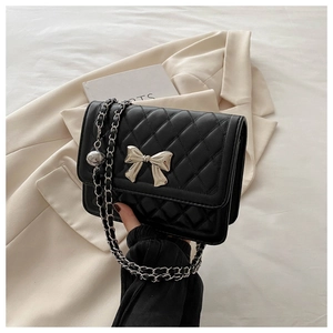 Detail of black quilted shoulder bag featuring silver bow clasp and chain strap on blazer