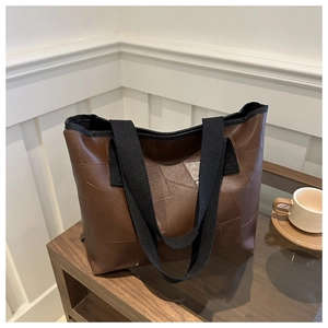Detail view of a large brown leather tote bag with unique patchwork and wide fabric strap