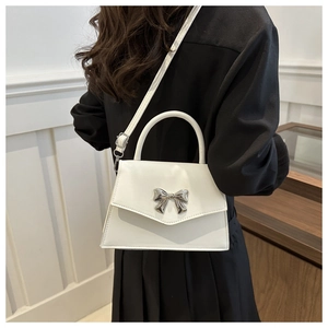 Detail of white mini square bag with silver metal bow and adjustable leather strap