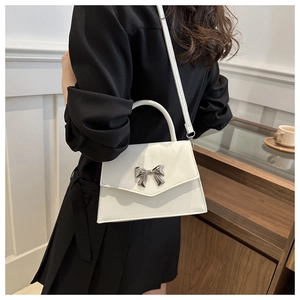 Model view of white crossbody bag with silver bow accent and top handle detail