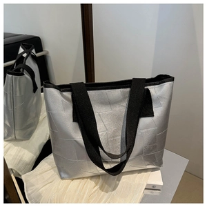 Detail of silver geometric tote bag featuring metallic patch design and black fabric straps