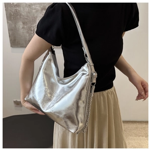Silver metallic hobo bag with embossed lettering shown as a shoulder bag on a model